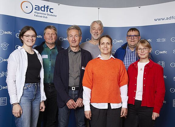 Ein Gruppenbild vor einem blauen Hintergund mit ADFC-Logos. Der neue ADFC-Bundesvorstand. Von links nach rechts: Lena Adam, Joachim Lohse, Christian Tänzler, Frank Masurat, Sarah Holczer, Christoph Schmidt und Vera Konrad. Nicht im Bild: Clara Bohle. 
